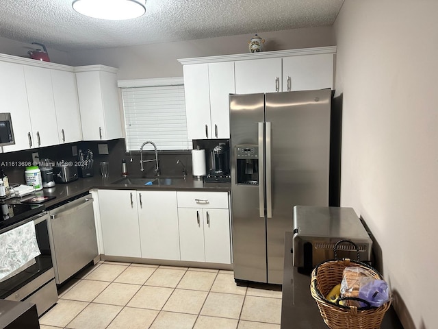 kitchen with appliances with stainless steel finishes, sink, white cabinets, and light tile flooring