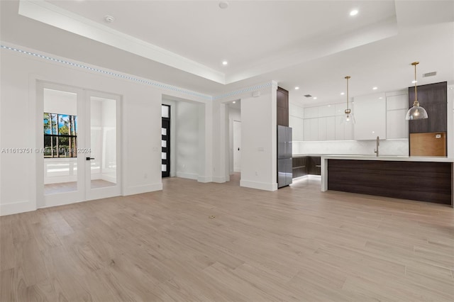 unfurnished living room featuring light hardwood / wood-style floors, sink, and a tray ceiling