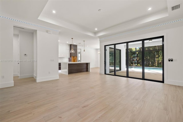 unfurnished living room featuring a raised ceiling, sink, and light hardwood / wood-style flooring