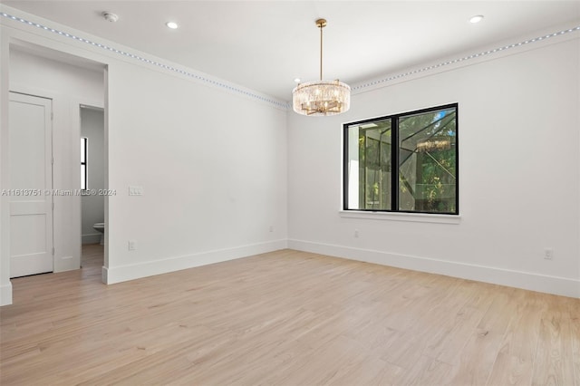 spare room featuring light wood-type flooring and an inviting chandelier