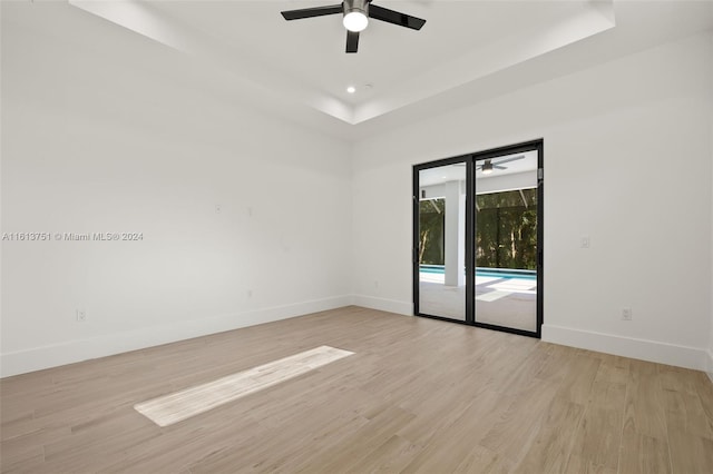 empty room featuring a tray ceiling, ceiling fan, and light wood-type flooring