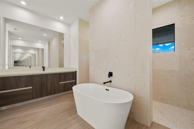 bathroom featuring separate shower and tub, vanity, and tile walls