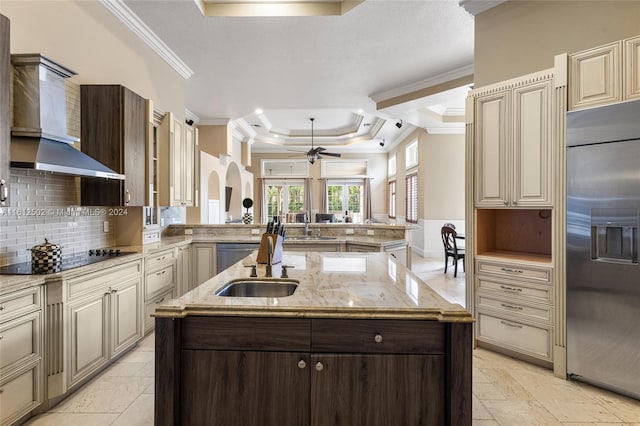 kitchen featuring appliances with stainless steel finishes, a kitchen island with sink, light stone counters, tasteful backsplash, and a raised ceiling