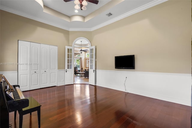 living area with ornamental molding, hardwood / wood-style floors, a towering ceiling, ceiling fan, and a raised ceiling