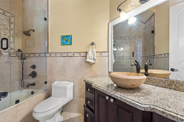 full bathroom with bath / shower combo with glass door, tile walls, toilet, and vanity