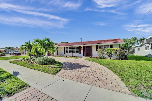 ranch-style house featuring a front lawn, decorative driveway, a tile roof, and stucco siding