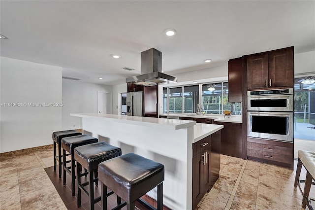 kitchen featuring a kitchen island, a kitchen breakfast bar, light countertops, appliances with stainless steel finishes, and island exhaust hood