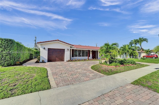 ranch-style home featuring a garage, a tile roof, decorative driveway, stucco siding, and a front lawn