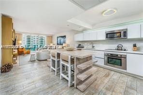 kitchen with appliances with stainless steel finishes, a breakfast bar area, white cabinets, and light hardwood / wood-style flooring