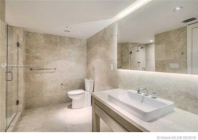 bathroom with vanity, a shower with shower door, tile walls, and toilet