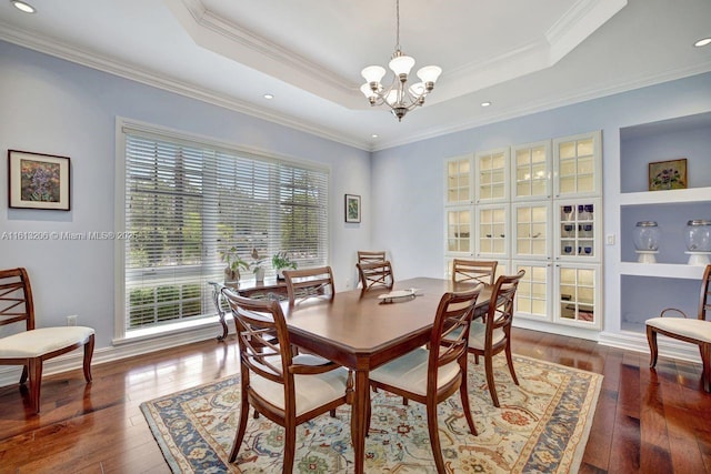 dining room featuring built in features, dark hardwood / wood-style flooring, a raised ceiling, crown molding, and an inviting chandelier