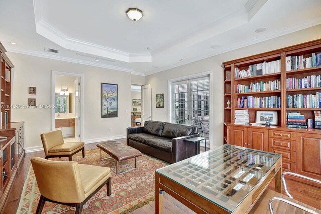 living room featuring crown molding, light hardwood / wood-style flooring, and a raised ceiling