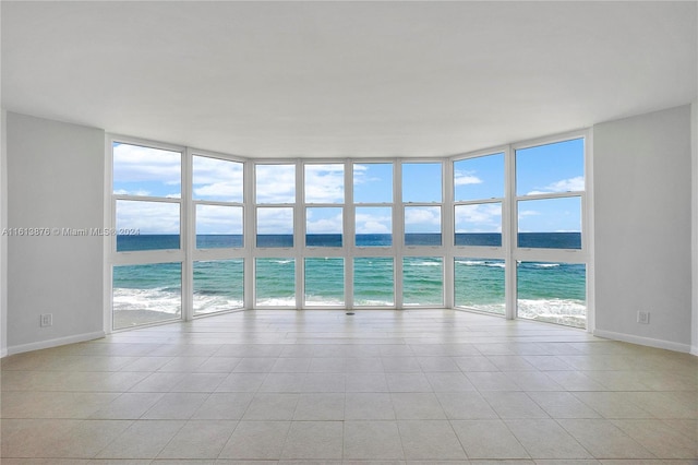 tiled empty room with a wealth of natural light, a water view, and expansive windows