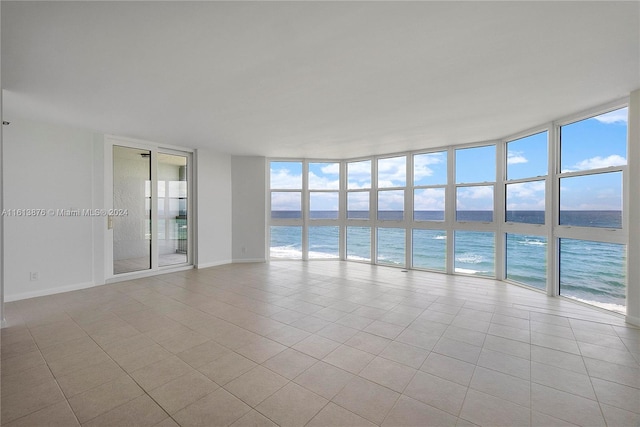 tiled empty room featuring a view of the beach, expansive windows, and a water view