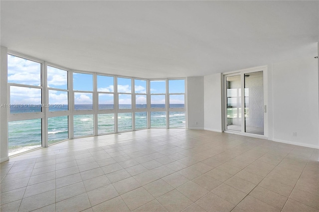 tiled spare room with a healthy amount of sunlight, floor to ceiling windows, and a water view