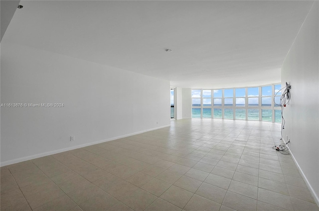 empty room with floor to ceiling windows, light tile flooring, and a water view