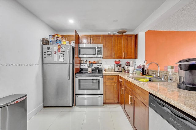 kitchen featuring light stone countertops, appliances with stainless steel finishes, light tile patterned floors, and sink