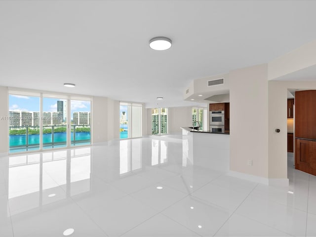 tiled empty room with a wealth of natural light, a water view, expansive windows, and sink