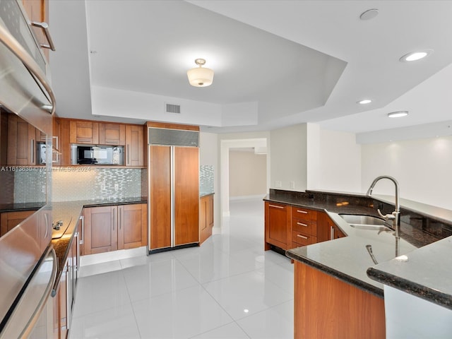 kitchen featuring kitchen peninsula, paneled built in fridge, light tile patterned floors, and sink