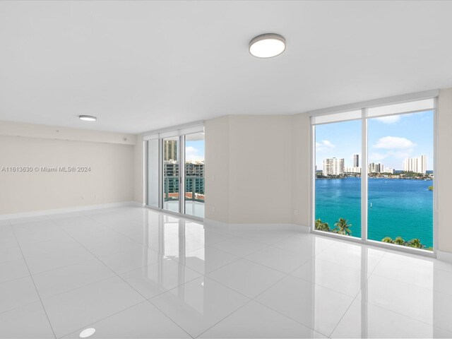 empty room featuring light tile patterned floors, a wall of windows, a water view, and plenty of natural light