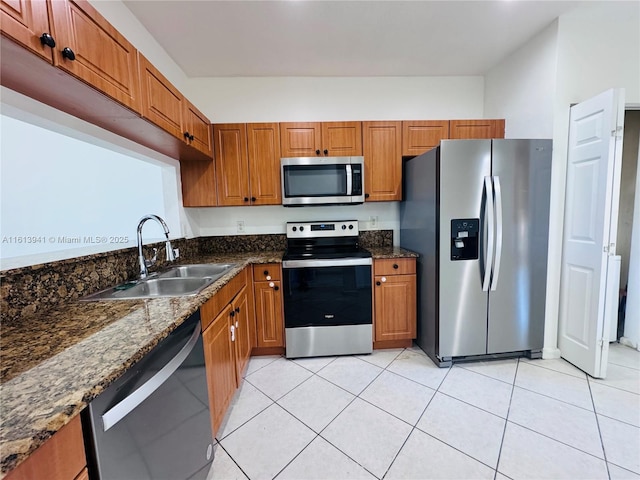 kitchen featuring light tile patterned flooring, appliances with stainless steel finishes, dark stone counters, and sink