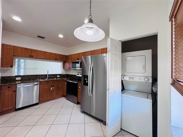 kitchen with sink, stacked washing maching and dryer, decorative light fixtures, light tile patterned flooring, and stainless steel appliances