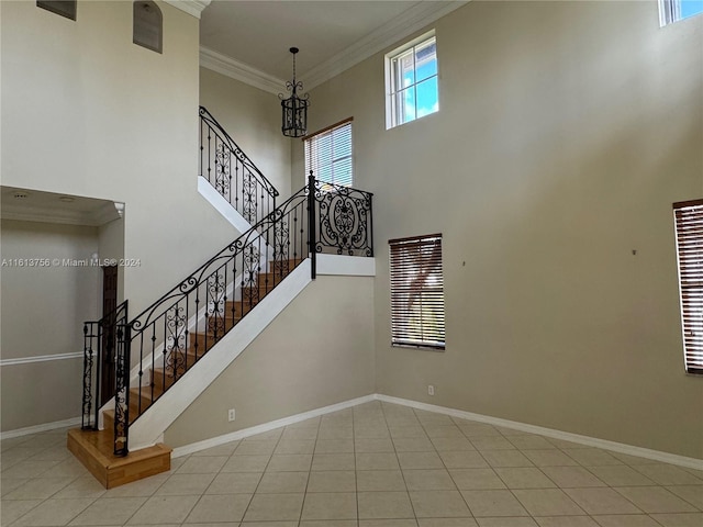 stairs featuring ornamental molding, a notable chandelier, light tile patterned floors, and a towering ceiling