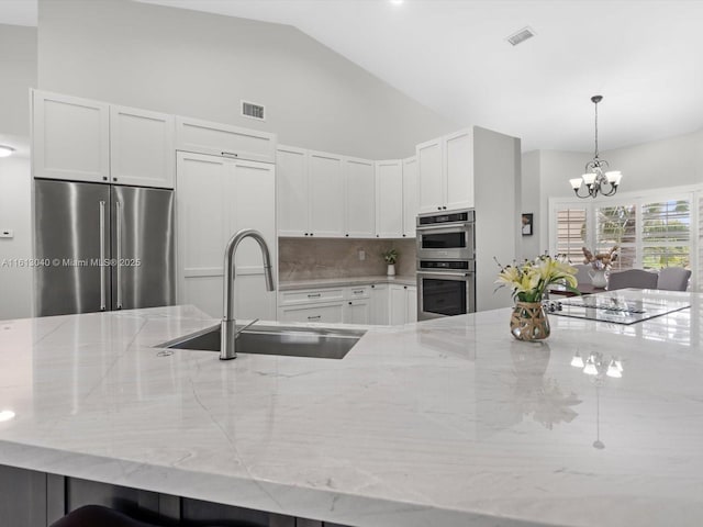 kitchen with stainless steel appliances, sink, backsplash, vaulted ceiling, and light stone counters