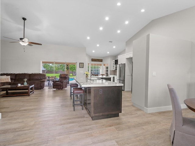 kitchen featuring white cabinetry, stainless steel refrigerator, sink, high vaulted ceiling, and a breakfast bar area