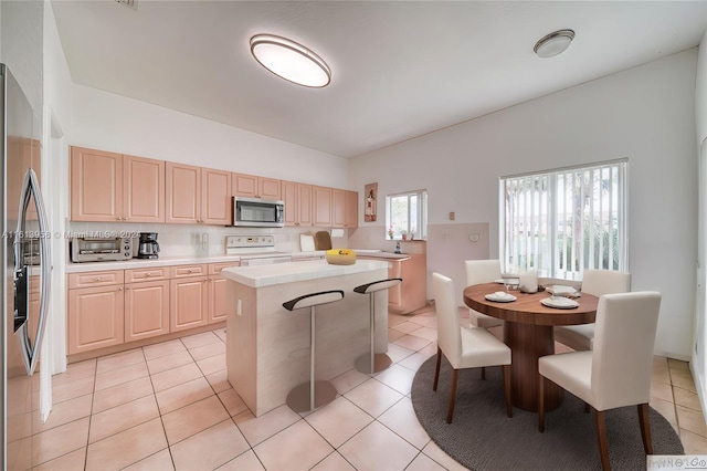 kitchen with light tile patterned flooring, stainless steel appliances, a center island, and light brown cabinetry