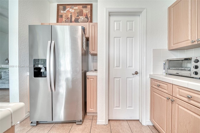 kitchen featuring light brown cabinetry, tasteful backsplash, stainless steel fridge, tile countertops, and light tile patterned floors