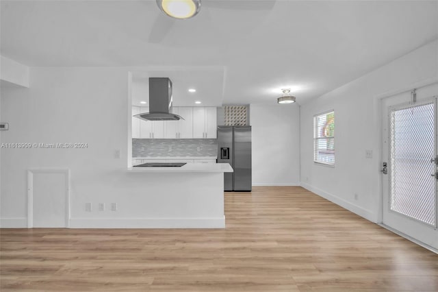 kitchen featuring tasteful backsplash, white cabinetry, island range hood, kitchen peninsula, and stainless steel fridge