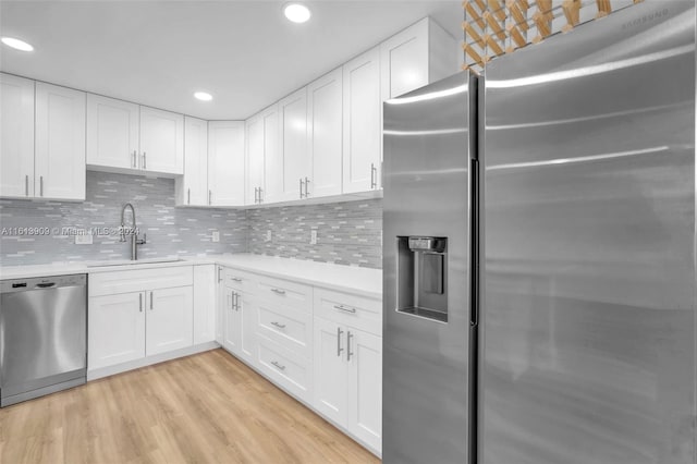 kitchen with appliances with stainless steel finishes, sink, white cabinets, light wood-type flooring, and decorative backsplash