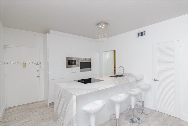 kitchen featuring stainless steel appliances, sink, light stone countertops, a breakfast bar, and white cabinets