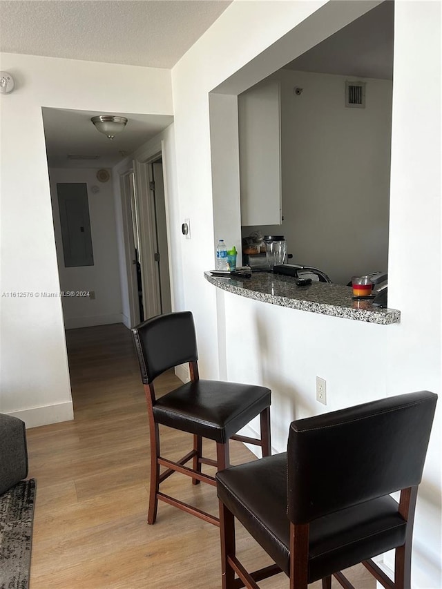 kitchen featuring light hardwood / wood-style floors, electric panel, and stone countertops