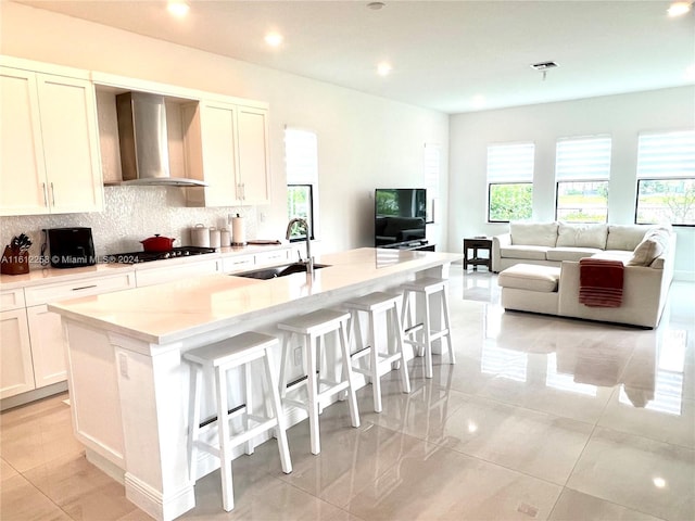 kitchen with a center island with sink, white cabinets, wall chimney range hood, sink, and stainless steel gas cooktop