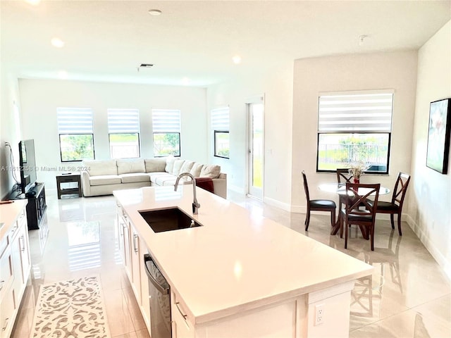 kitchen featuring sink, light tile patterned floors, stainless steel dishwasher, a center island with sink, and white cabinets