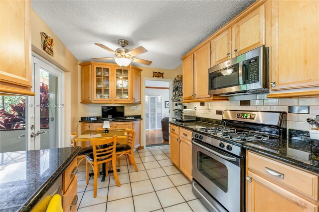 kitchen with dark stone countertops, decorative backsplash, light tile patterned floors, and stainless steel appliances