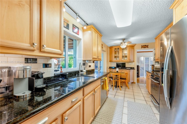 kitchen with appliances with stainless steel finishes, a textured ceiling, sink, light tile patterned floors, and dark stone countertops