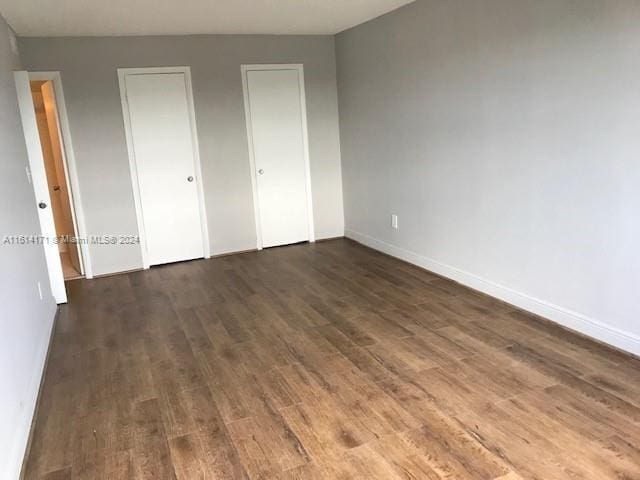 unfurnished bedroom featuring multiple closets and dark hardwood / wood-style floors