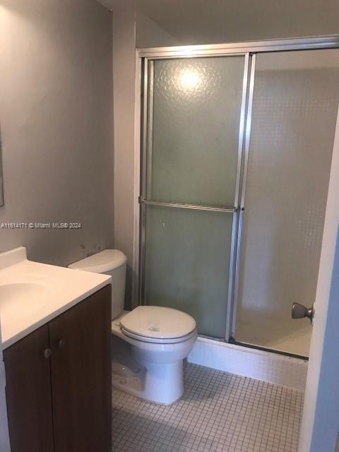 bathroom with vanity, toilet, a shower with shower door, and tile patterned flooring