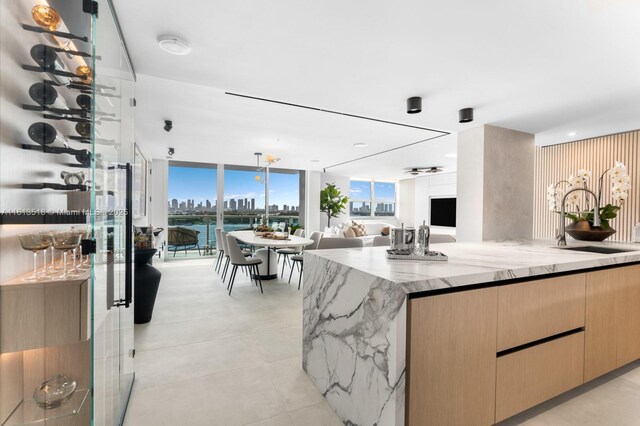 kitchen with light brown cabinetry, sink, ceiling fan, light stone counters, and floor to ceiling windows