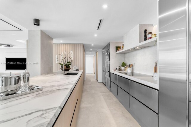 kitchen with light stone counters, black electric cooktop, and built in fridge