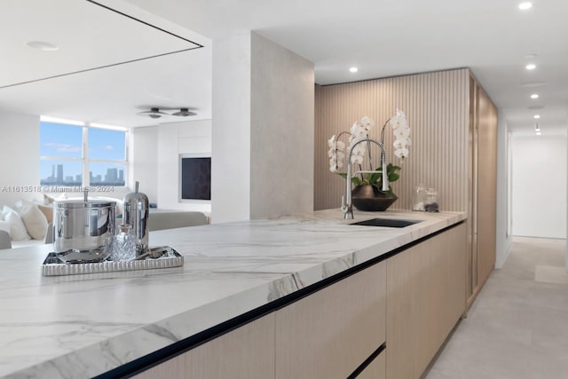 kitchen with ceiling fan, light stone countertops, sink, and light brown cabinetry