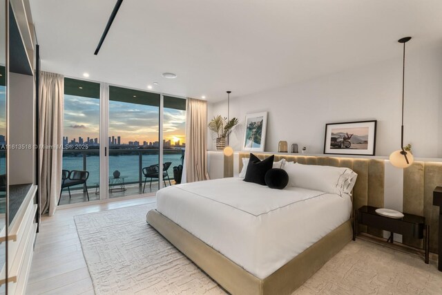 bedroom featuring expansive windows, a water view, light hardwood / wood-style flooring, and access to outside