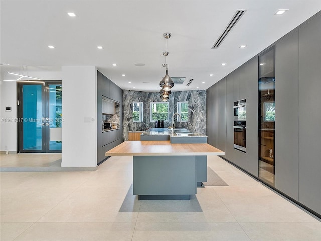 kitchen featuring pendant lighting, sink, gray cabinetry, a kitchen island with sink, and french doors