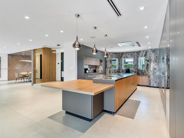 kitchen featuring wood counters, sink, gray cabinetry, a large island with sink, and hanging light fixtures