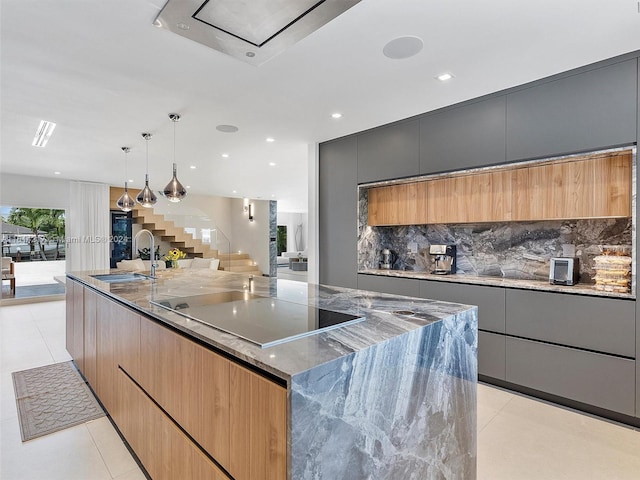 kitchen featuring sink, dark stone countertops, black electric stovetop, decorative light fixtures, and a large island with sink