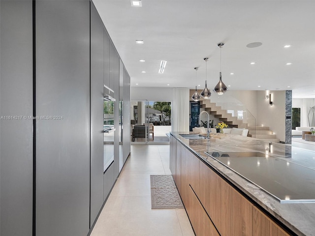 kitchen featuring sink, light stone counters, stainless steel oven, hanging light fixtures, and light tile patterned floors