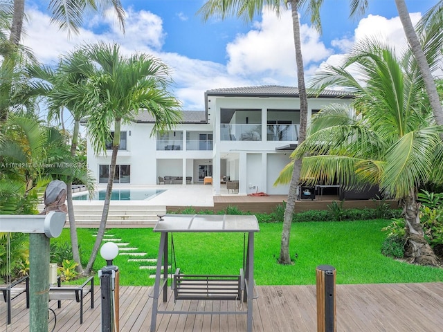 rear view of house with a balcony, a swimming pool side deck, and a yard